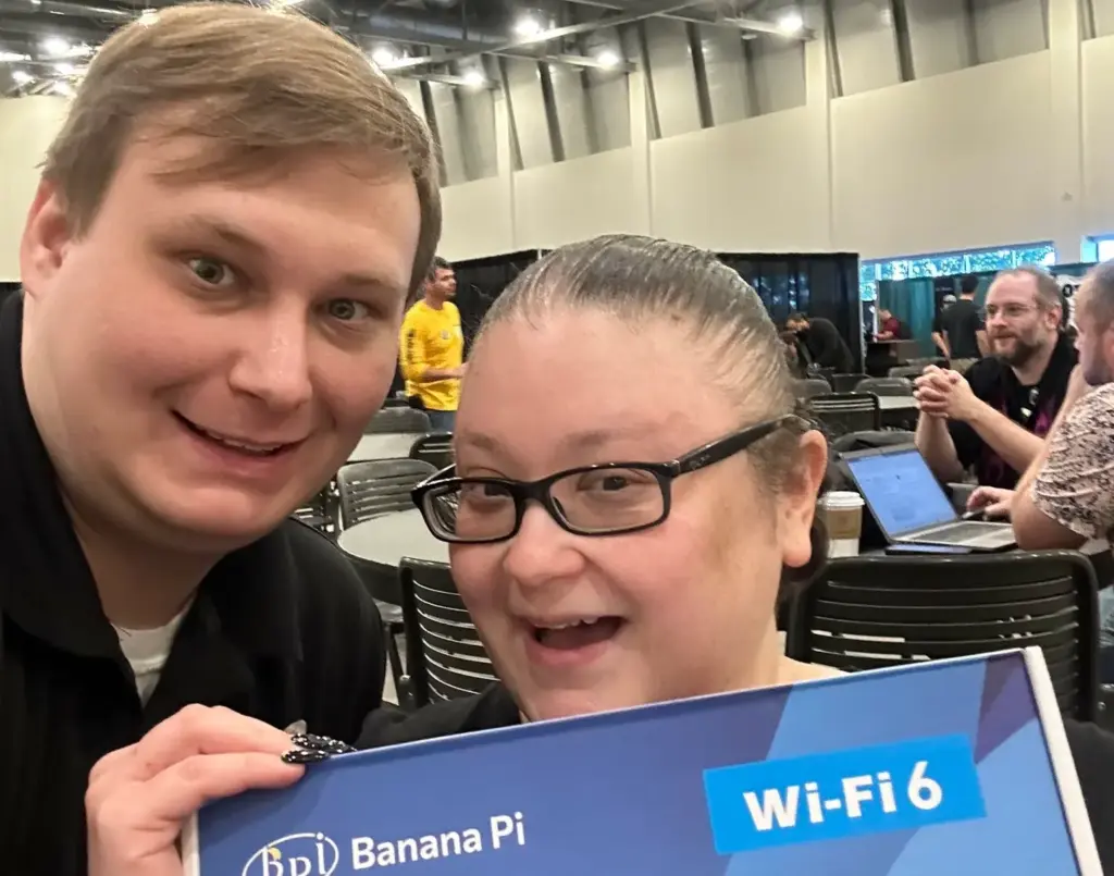 sysadminafterdark and mandolinsara pose at GrrCon 2023 with a BananaPi router. 